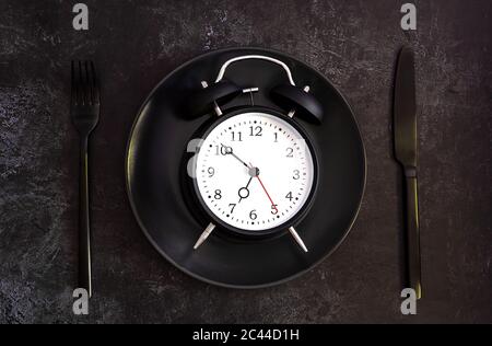 Black alarm clock on a black plate with black knife and fork.  Stock Photo