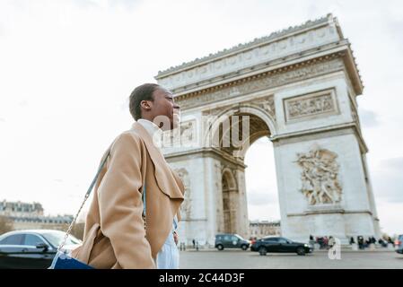 Happy young woman against Arc de Triomphe during sunny day, Paris, France Stock Photo