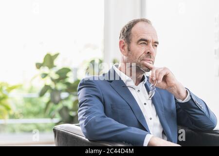 Portrait of pensive businessman sitting in armchair looking at distance Stock Photo