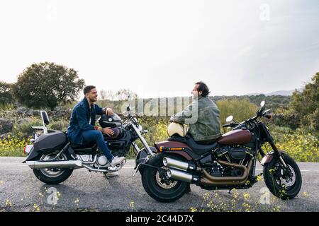 Male bikers talking while sitting on motorcycles against sky Stock Photo