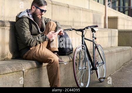 Side view of bearded mid adult man using smart phone while sitting on steps in city Stock Photo