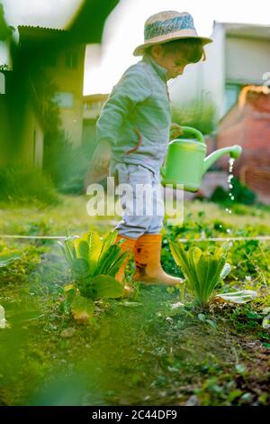 Full length side view of cute girl with watering can standing by plants at orchard Stock Photo