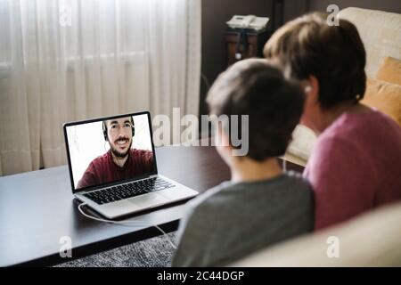 Grandson using a laptop with his grandmother for video chat with his father Stock Photo