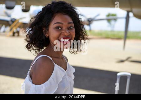 Side view portrait of smiling young woman standing at airport runway Stock Photo