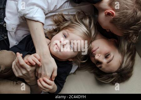 Directly above view of blond boy lying with brother and mother on sofa at home