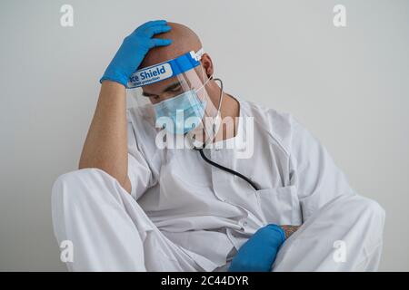 Exhausted man in protective wear sitting on the floor Stock Photo