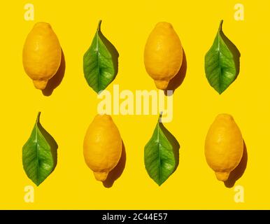 Pattern of ripe lemons and green leaves against yellow background Stock Photo