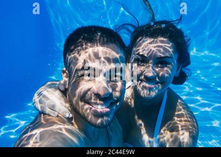 Smiling young couple swimming underwater in pool Stock Photo