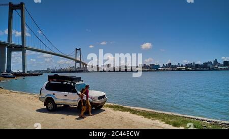 Mozambique, Katembe, Adult couple standing by 4x4 car admiring view of Maputo Bay with city and Maputo-Katembe Bridge in background Stock Photo