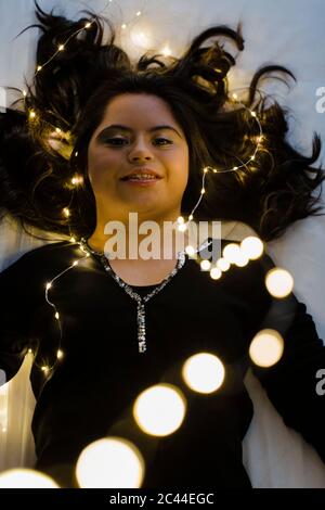 Confident young woman with down syndrome lying on illuminated bed at home Stock Photo