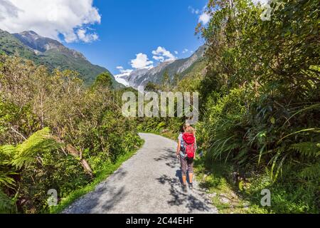 New Zealand, Westland District, Franz Josef, Female backpacker taking break on scenic road leading to Franz Josef Glacier Stock Photo