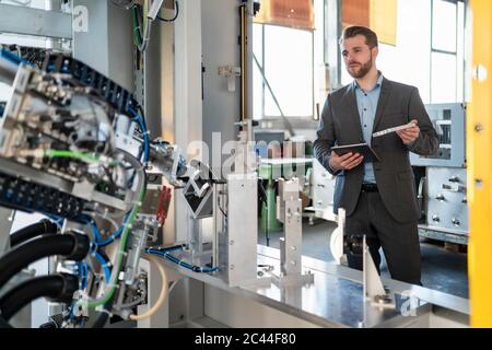 Young businessman with tablet and workpiece at a machine in a factory Stock Photo
