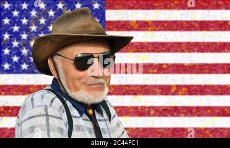 Portrait of not a young man in a cowboy hat and glasses with a gray beard against the background of the USA flag. Stock Photo