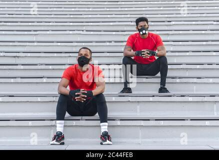 Two sportsmen wearing masks sitting on stairs Stock Photo