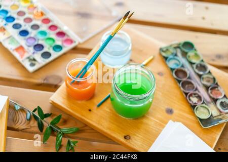 Watercolor paints with water and paintbrushes on wooden table home Stock Photo