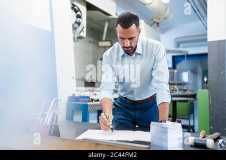 Businessman working on a plan in factory hall Stock Photo