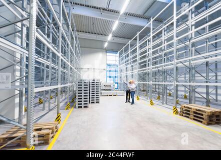 Two men wearing hard hats talking in storehouse of a factory Stock Photo