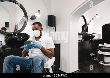 Barber wearing surgical mask and gloves using smartphone Stock Photo