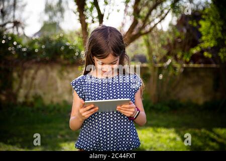 Smiling girl standing in the garden using digital tablet Stock Photo