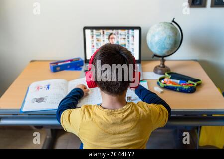 Rear view of boy listening to teacher through video call at home during pandemic outbreak Stock Photo
