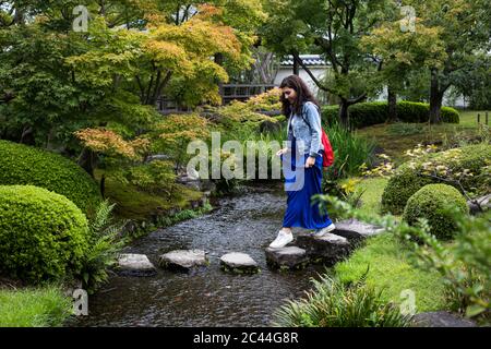 Japan, Kyoto, Woman on stepping stones in pond Stock Photo