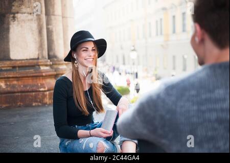 Happy young woman looking at man while listening music in city Stock Photo