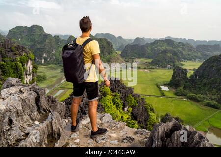 Vietnam, Ninh Binh Province, Ninh Binh, Male hiker admiring scenic landscape of Hong River Delta from top of karst formation