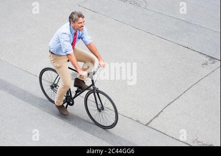 Smiling businessman riding bicycle on street in city Stock Photo