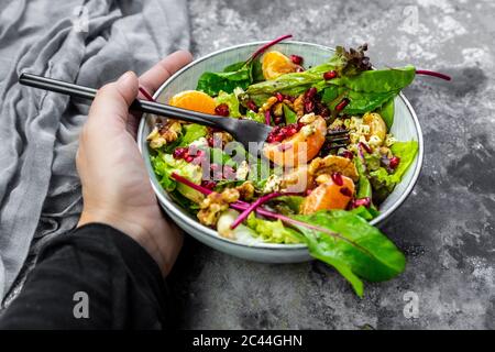 Hand holding bowl of winter salad with lettuce, tangerines, walnuts, feta and pomegranate seeds Stock Photo