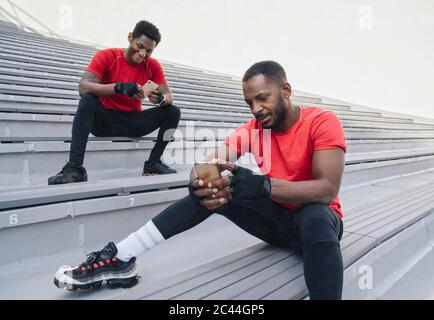 Two sportsmen sitting on stairs in a stadium using smartphones Stock Photo