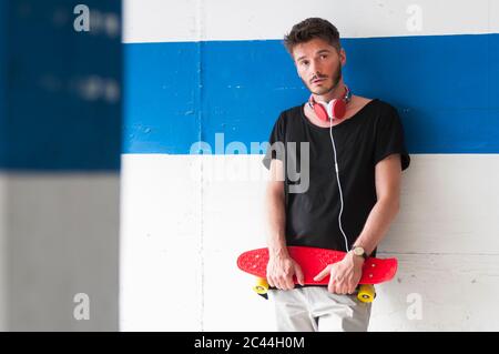 Portrait of man with skateboard leaning against wall Stock Photo