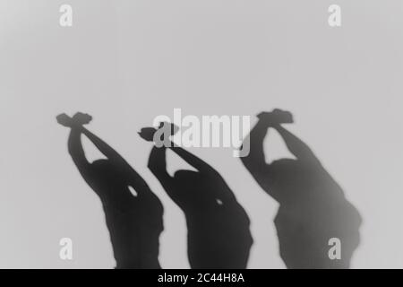 Three man crossing hands and raising fists in protest, silhouette on white wall Stock Photo