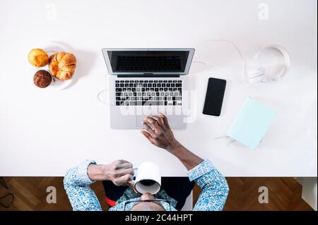 Young man drinking coffee while using laptop at home office desk Stock Photo