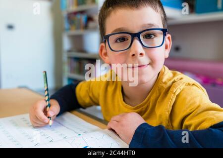 Cute boy doing homework while sitting at desk during coronavirus Stock Photo