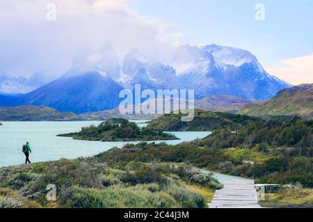 Chile, Ultima Esperanza Province, Male backpacker hiking along shore of Lake Pehoe with Cuernos del Paine in background Stock Photo