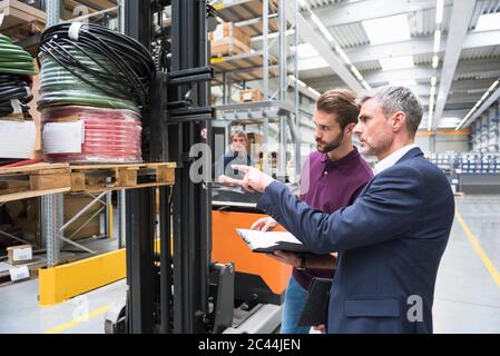 Two men and worker on forklift in high rack warehouse Stock Photo