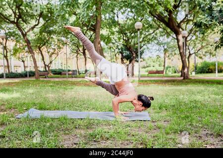 Mid adult woman practising yoga on mat in park, crow pose Stock Photo