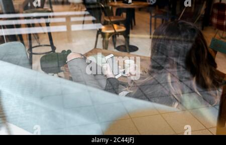 Woman using smartphone in coffee shop, seen through windowpane Stock Photo