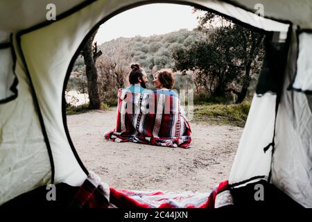 Couple wrapped in a blanket camping at lakeside Stock Photo