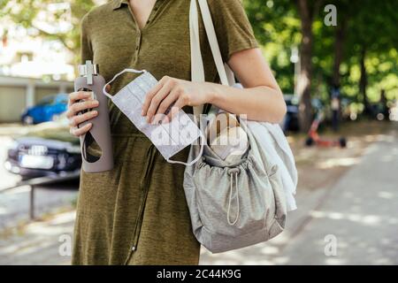 Close-up of woman holding a face mask and drinking bottle in her hand while walking to her health club Stock Photo