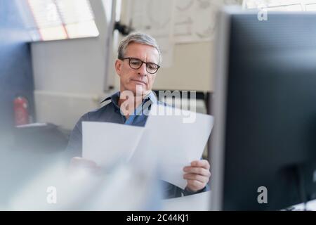 Confident mature male professional reading document while sitting at desk in office Stock Photo