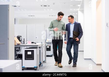 Two businessmen with tablet walking and talking in office Stock Photo