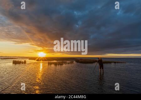 New Zealand, Tasman District, Puponga, Rear view of woman photographing cloudy sunrise over Golden Bay Stock Photo