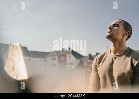 Young man standing on balcony, relaxing Stock Photo