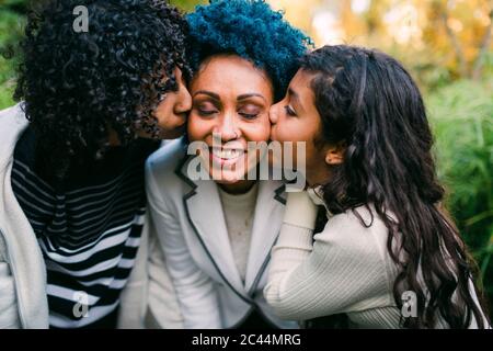 Loving children kissing on smiling mother's cheeks in park Stock Photo