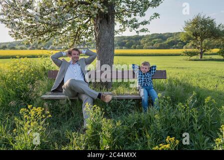 Relaxed man sitting with son on bench at park Stock Photo