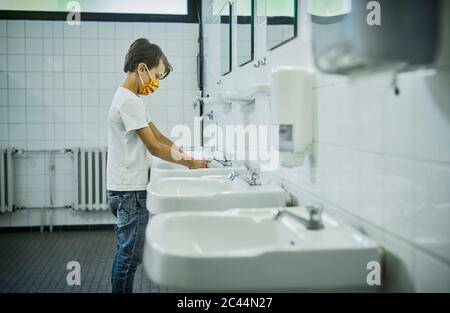 Boy wearing mask on school toilet washing his hands Stock Photo