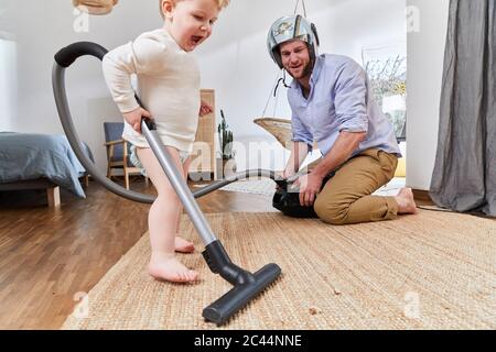 Cute baby boy cleaning carpet with vacuum cleaner by father in living room at home Stock Photo