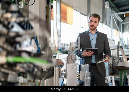 Young businessman with tablet and workpiece at a machine in a factory Stock Photo