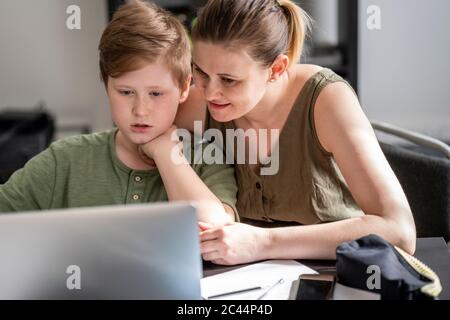 Mother homeschooling her son and using laptop at home Stock Photo